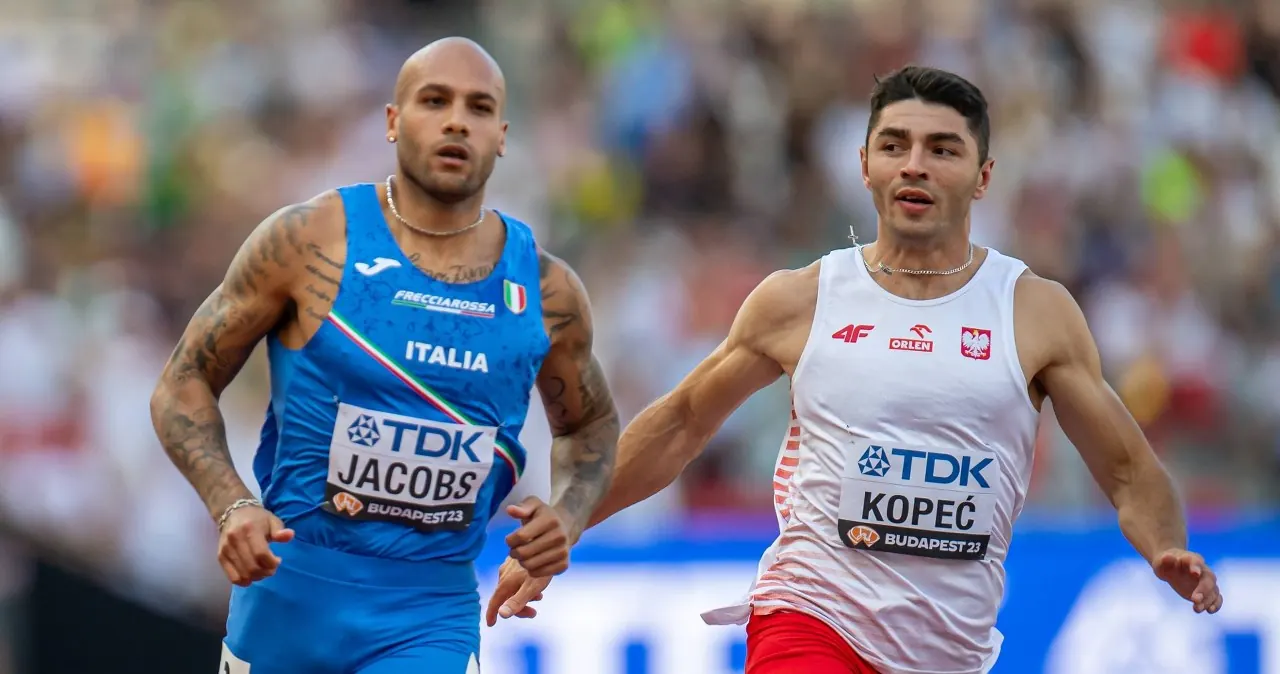 Dominik Kopeć w dynamicznej pozie podczas biegu na 100 metrów, na tle trybun stadionu.