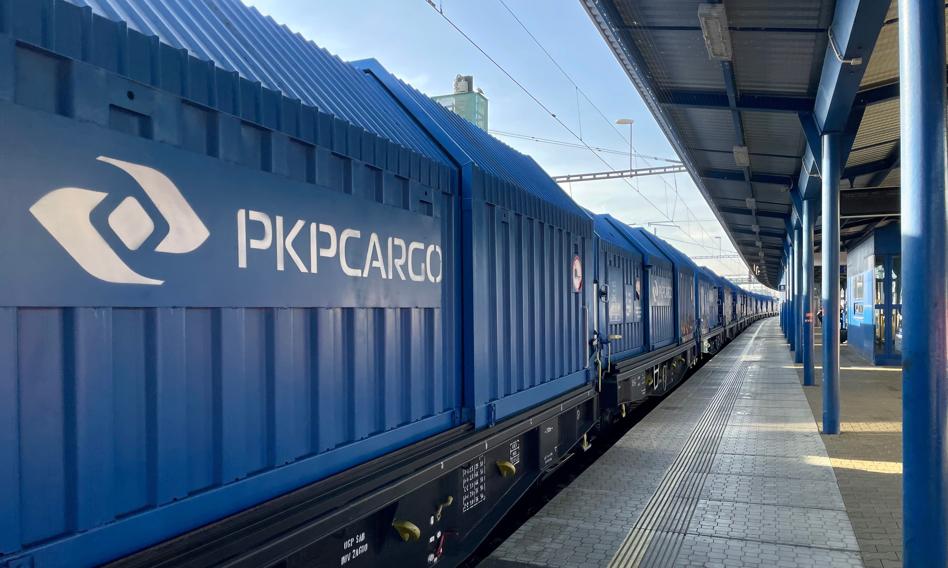 Pociąg towarowy PKP Cargo z wagonami wypełnionymi kruszywem przejeżdżający przez port lub plac budowy.