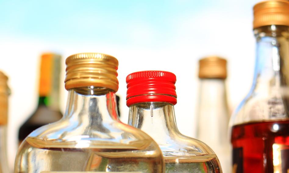 Butelki po alkoholach typu "małpki" na tle symbolu recyklingu, co symbolizuje wyzwania związane z włączeniem ich do systemu kaucyjnego.