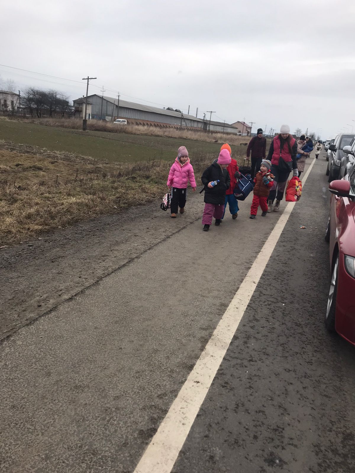 Grupa ludzi przekraczających granicę, z flagami Polski i Ukrainy w tle, symbolizująca kwestię uchodźców.