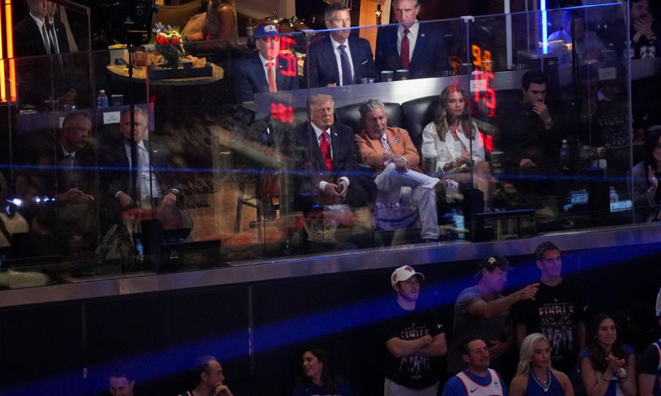 Donald Trump w loży podczas meczu finałowego NBA w Nowym Jorku, na ekranie w tle widać zbliżenie na jego twarz.