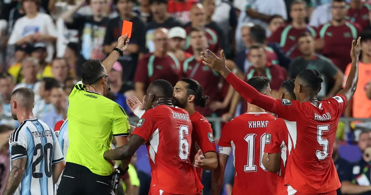 Breel Embolo, piłkarz, po otrzymaniu czerwonej kartki, z widocznym rozczarowaniem na twarzy, w tle sędzia i zawodnicy.