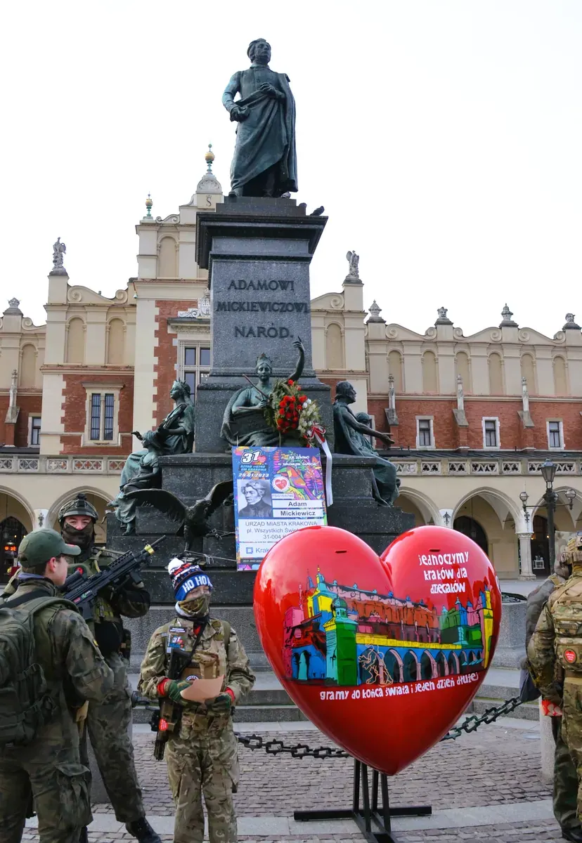 Tłum ludzi gromadzący się na Rynku Głównym w Krakowie, z widocznymi zabytkowymi kamienicami w tle, podczas zapowiadanej nieoficjalnej imprezy.
