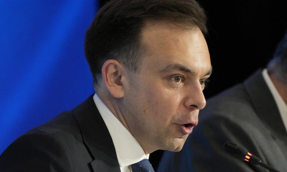 Minister finansów i gospodarki Andrzej Domański podczas wystąpienia, z widocznymi za nim symbolami polskiej flagi.