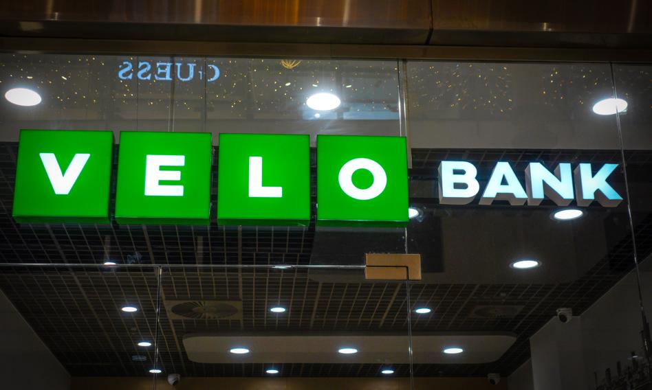 Logo VeloBank na tle fasady nowoczesnego budynku bankowego, symbolizujące zmiany strukturalne i procesy integracyjne w sektorze finansowym.