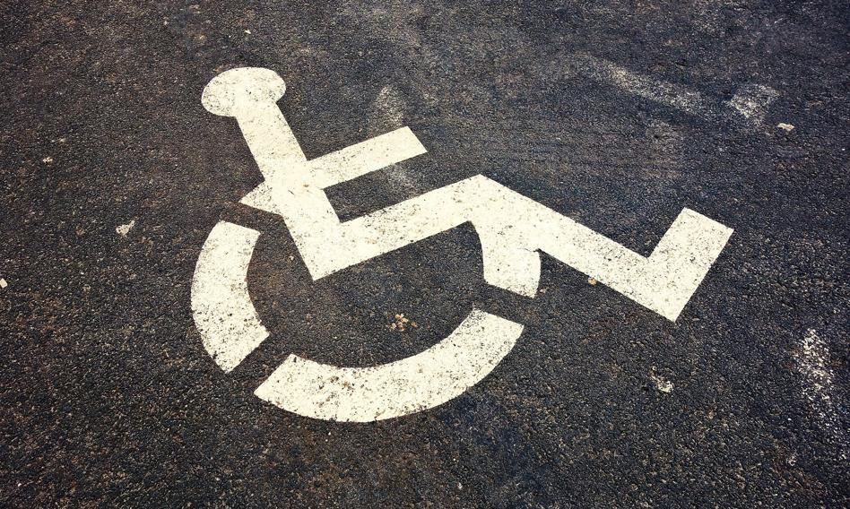 Osoba na wózku inwalidzkim próbująca wjechać do urzędu, którego wejście jest zablokowane schodami bez podjazdu