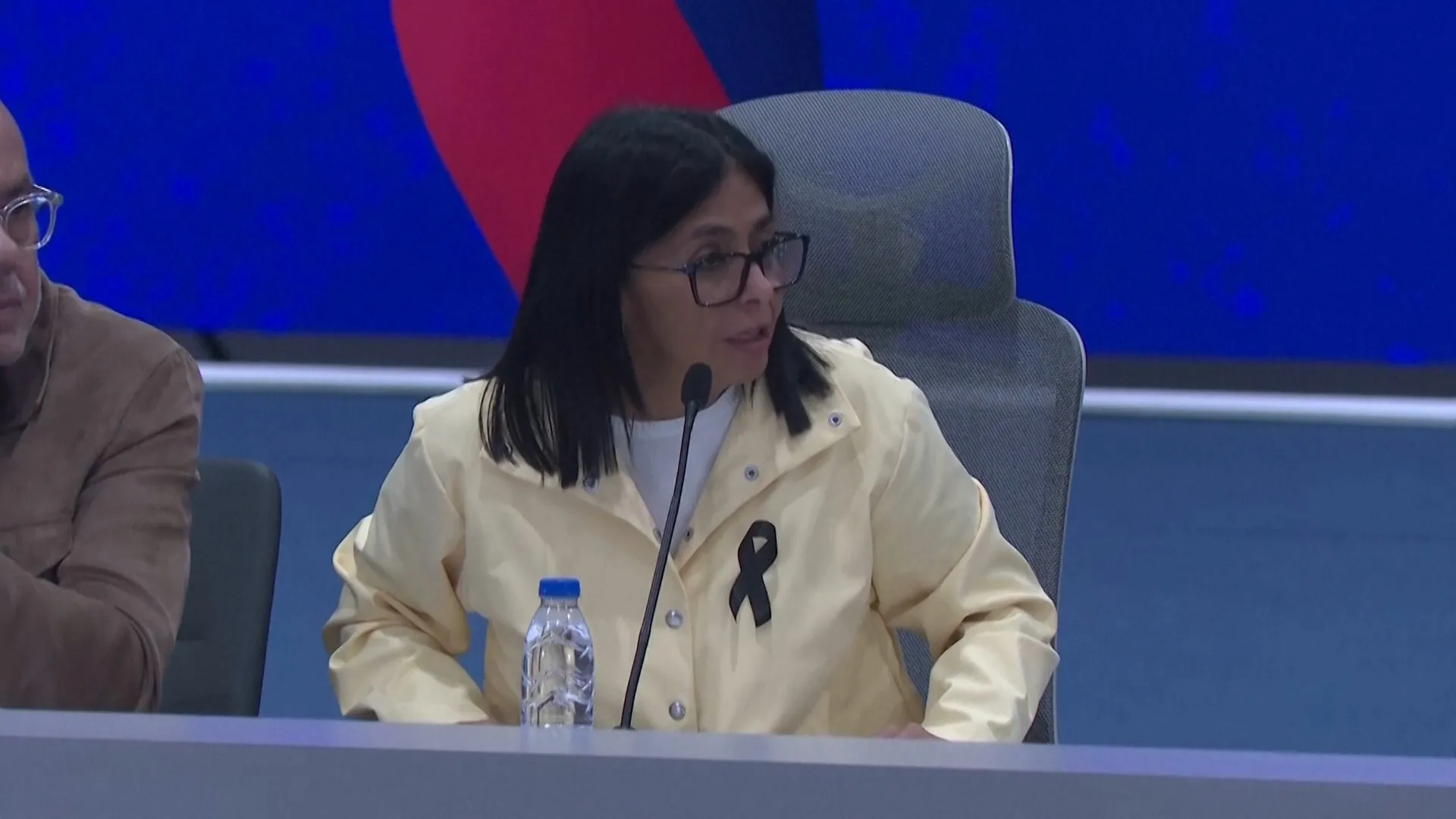 Delcy Rodríguez, pełniąca obowiązki prezydenta Wenezueli, podczas konferencji prasowej, z tłem sugerującym sytuację kryzysową.